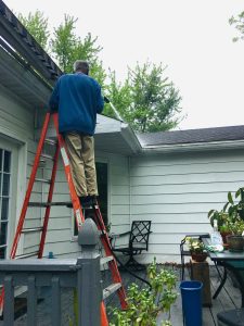 man on a ladder cleaning roofing gutter
